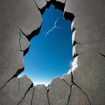 cracked concrete wall with a hole in the middle of it and a bright blue sky in the background