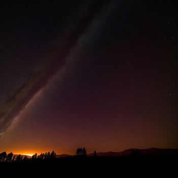 long exposure of a star in the sky above a field with trees and a hill in the background