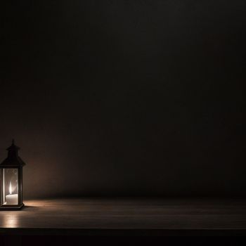 lit lantern on a table in a dark room with a dark background and a light shining on the floor