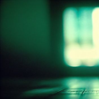 close up of a laptop keyboard with a blurry background of a window in the background and a light shining on the keyboard