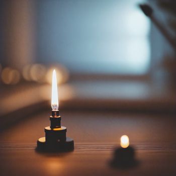 small candle is lit on a table with a blurry background of a room and a window in the background