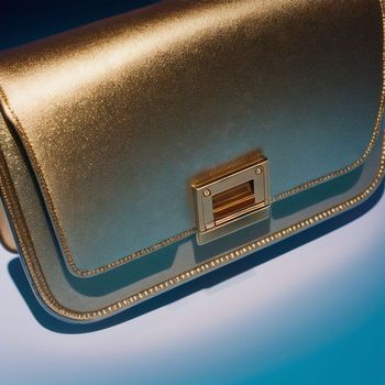 shiny gold purse sitting on top of a blue table top next to a blue wall