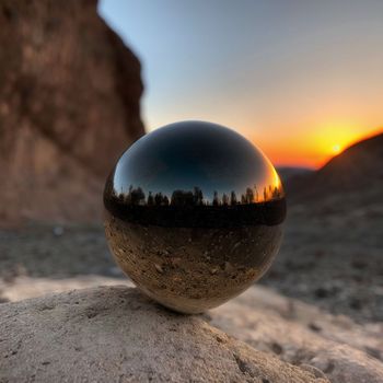 glass ball sitting on top of a rock in front of a sunset