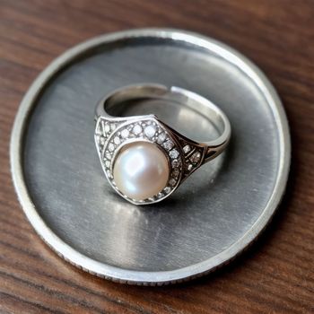 pearl and diamond ring sitting on top of a metal tray on a table